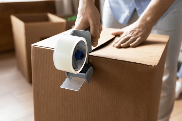 A person is holding a roll of tape on top of a box.