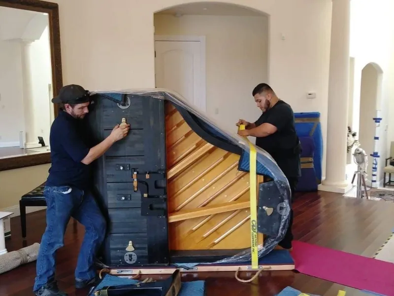 Two men are working on a piano.